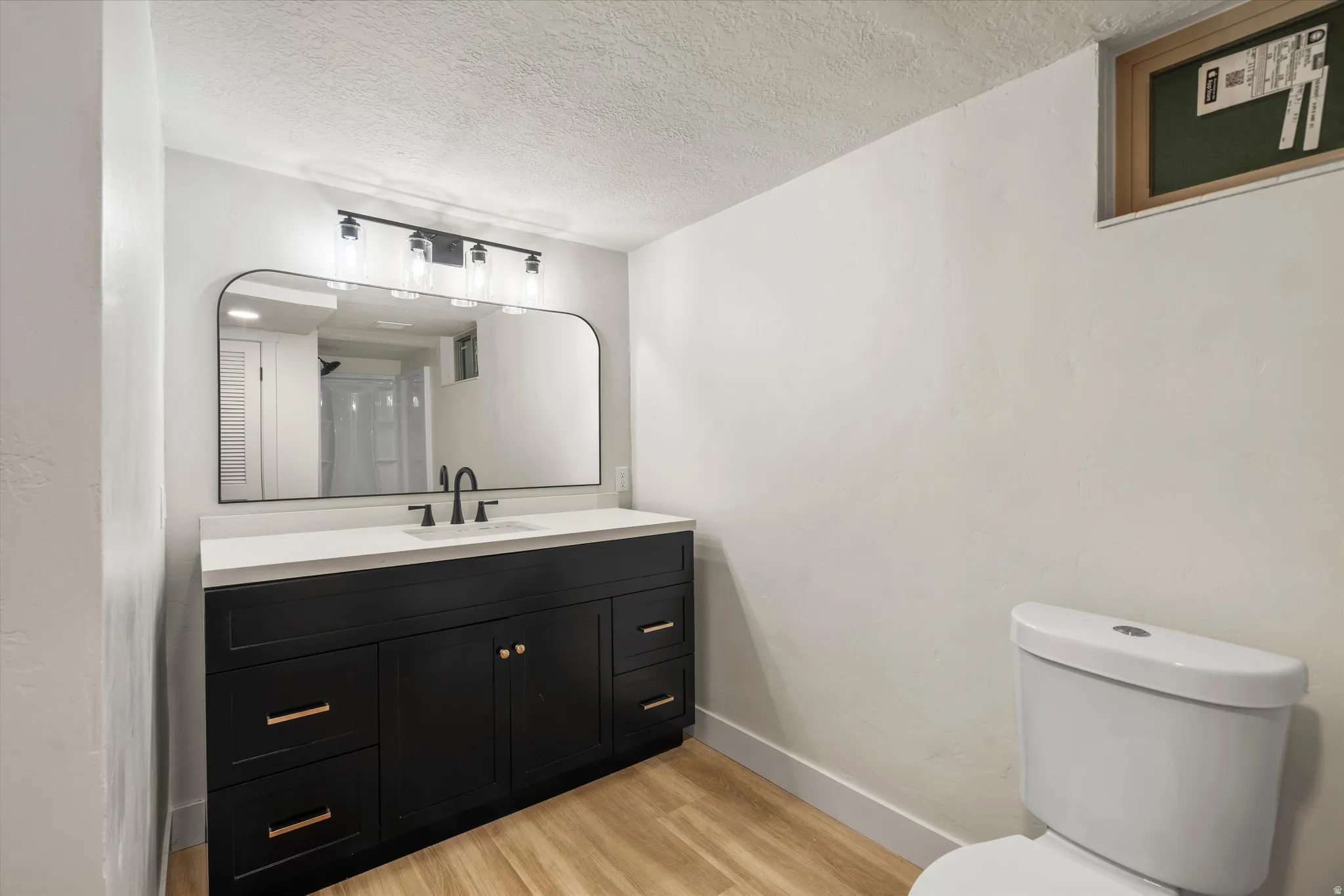 Contemporary bathroom featuring a black vanity with gold-tone hardware, white countertop, and a large arched mirror
