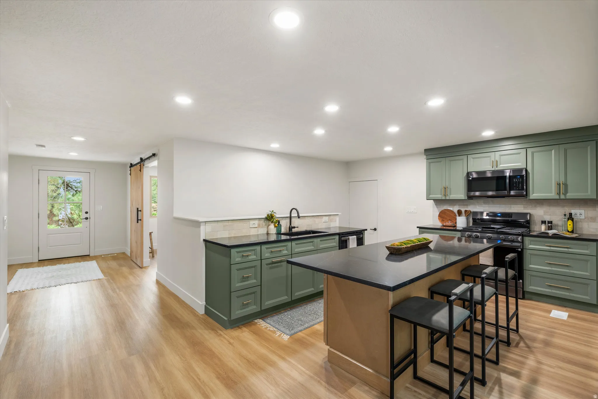 Open-concept kitchen featuring sage green cabinetry, black countertops, and a full suite of black stainless steel appliances