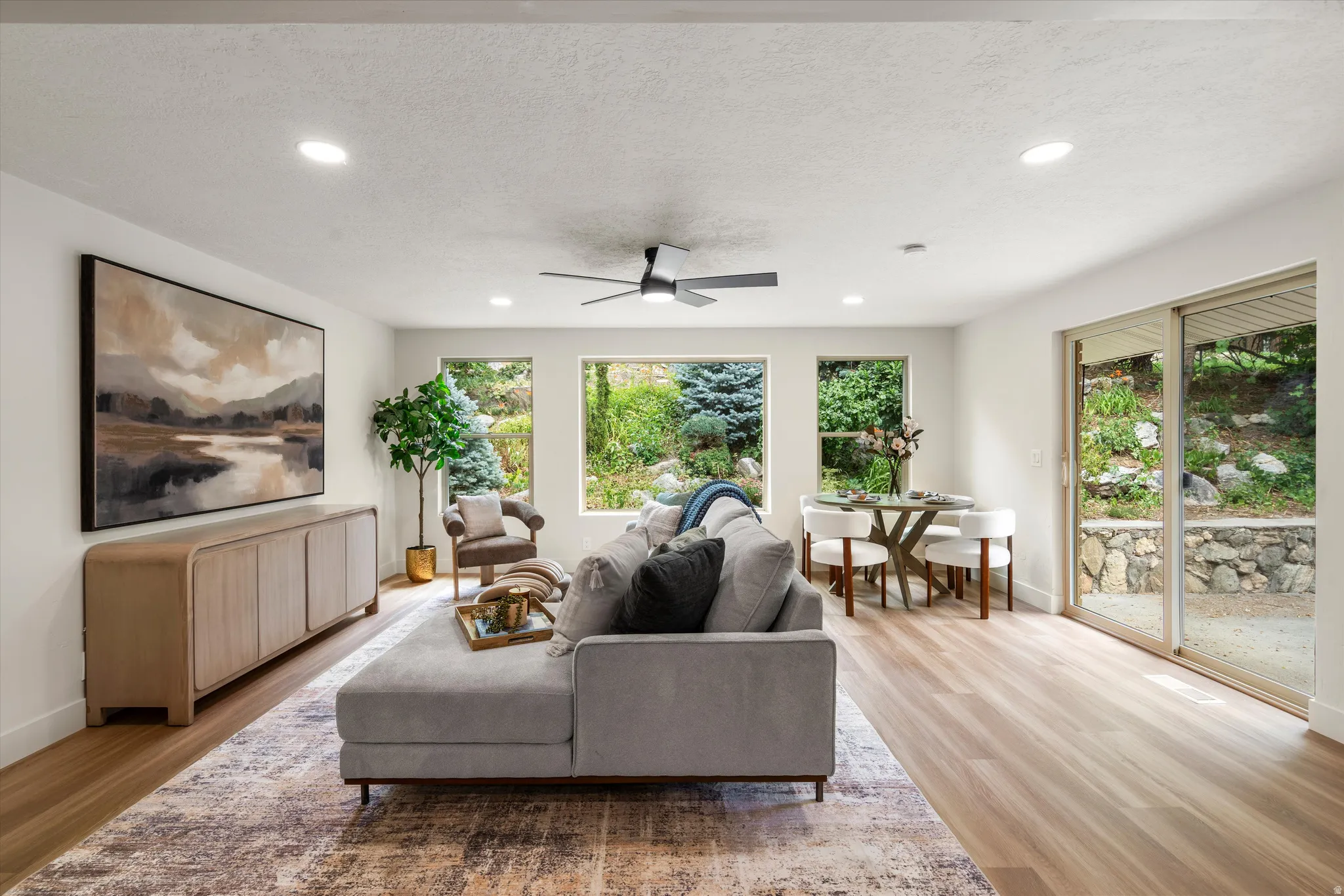Open-concept living space featuring recessed lighting, wood-finish flooring, a contemporary ceiling fan, three expansive windows, and sliding glass doors opening to the outdoors