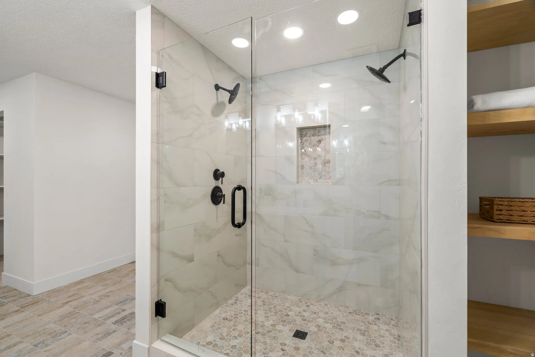 Glass-enclosed shower with a pebble floor, tile walls, and a recessed niche