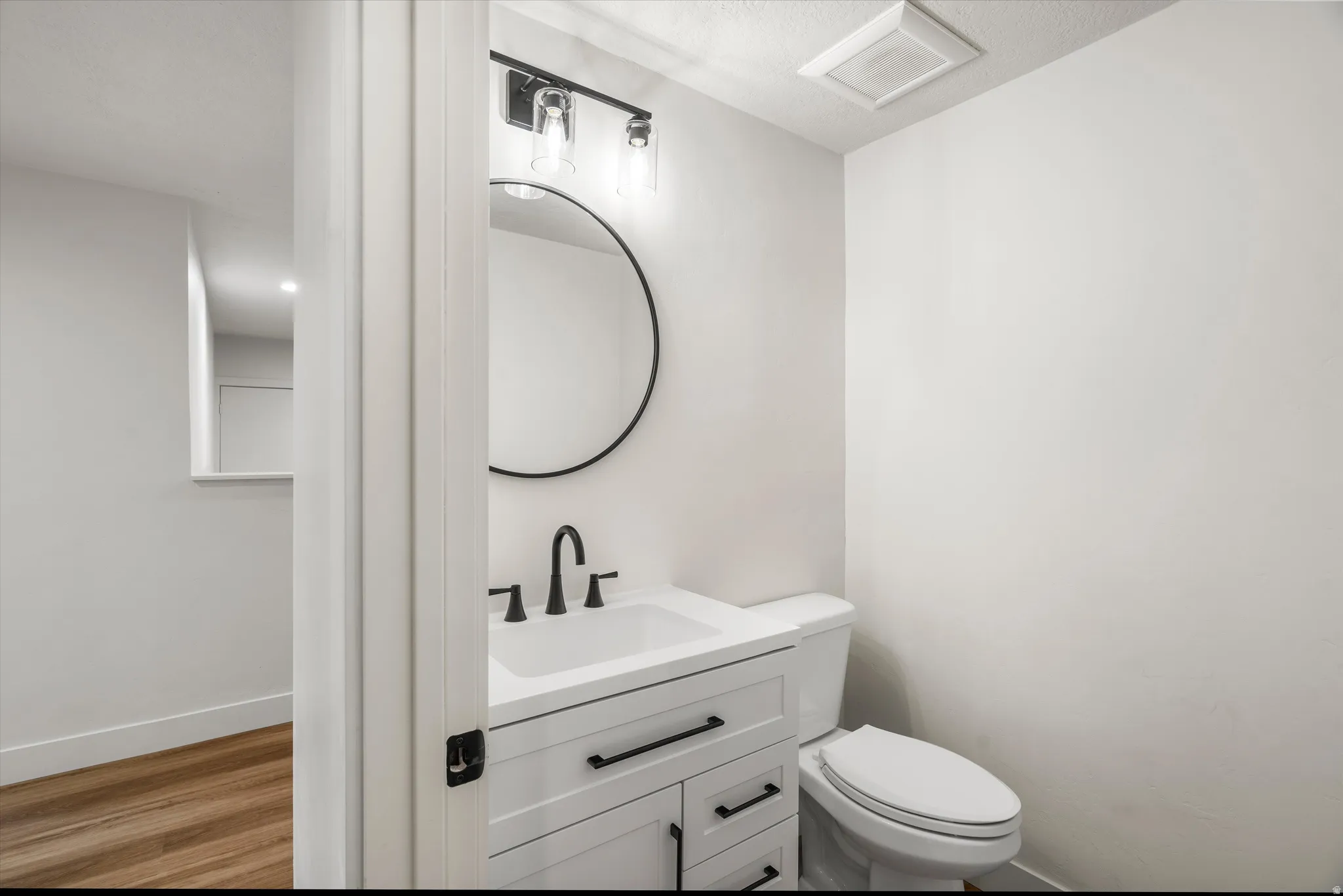 Bathroom featuring a white vanity with black hardware, a circular mirror, and a modern light fixture with exposed bulbs