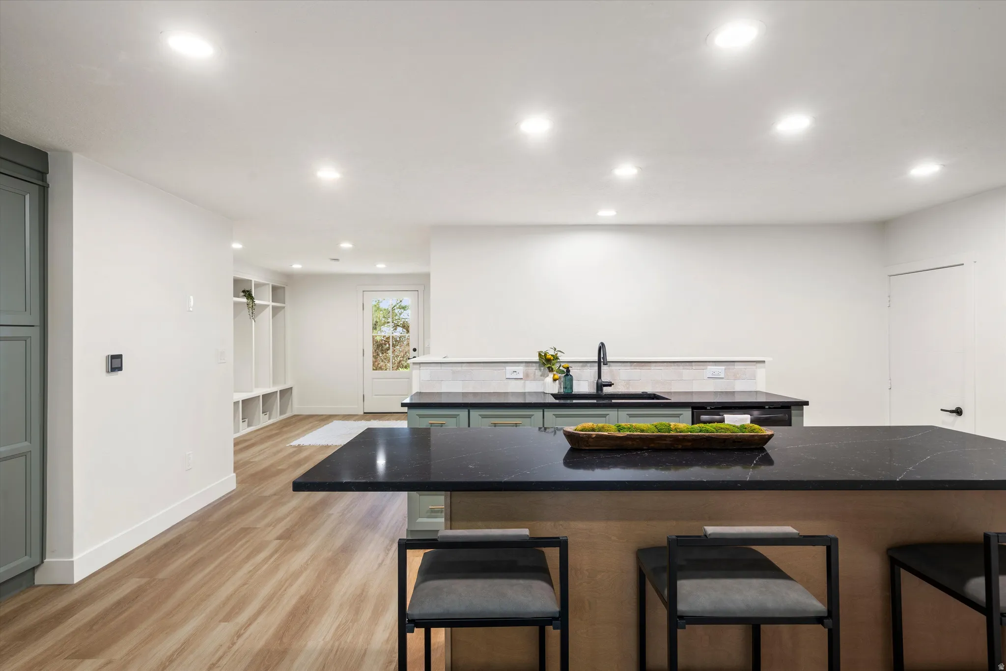 Kitchen island featuring a dark countertop with seating, wood-finish flooring, recessed lighting, light-toned walls, and a built-in storage area