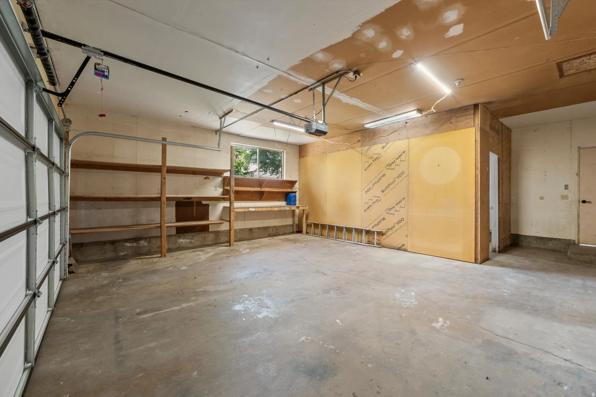 Spacious garage featuring a concrete floor, built-in wooden shelving, a single window, and fluorescent overhead lighting