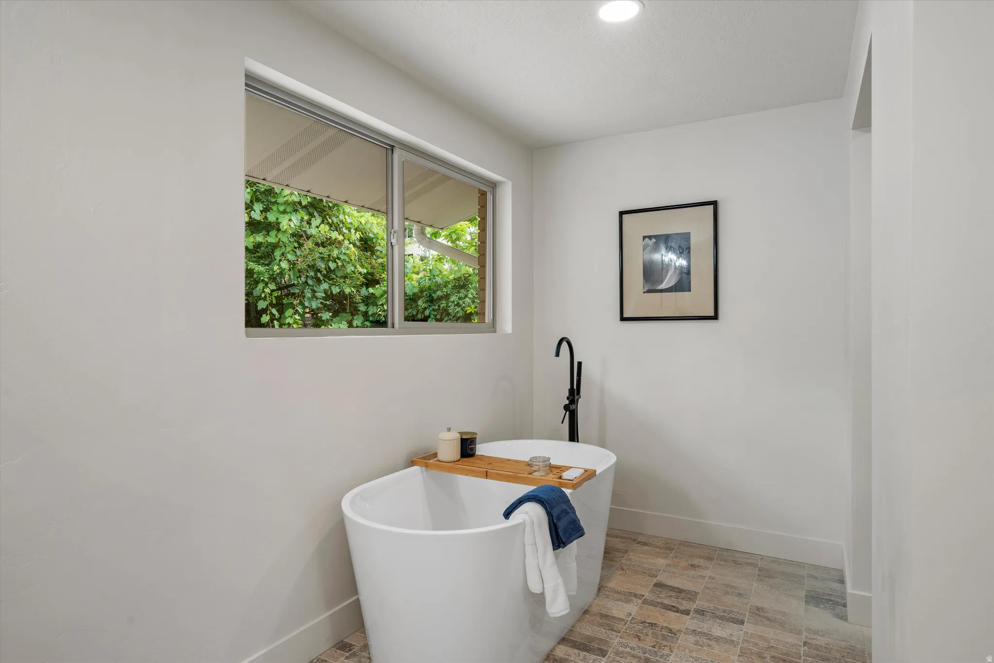 Freestanding soaking tub featuring a matte black floor-mounted faucet, complemented by multi-toned square tile flooring