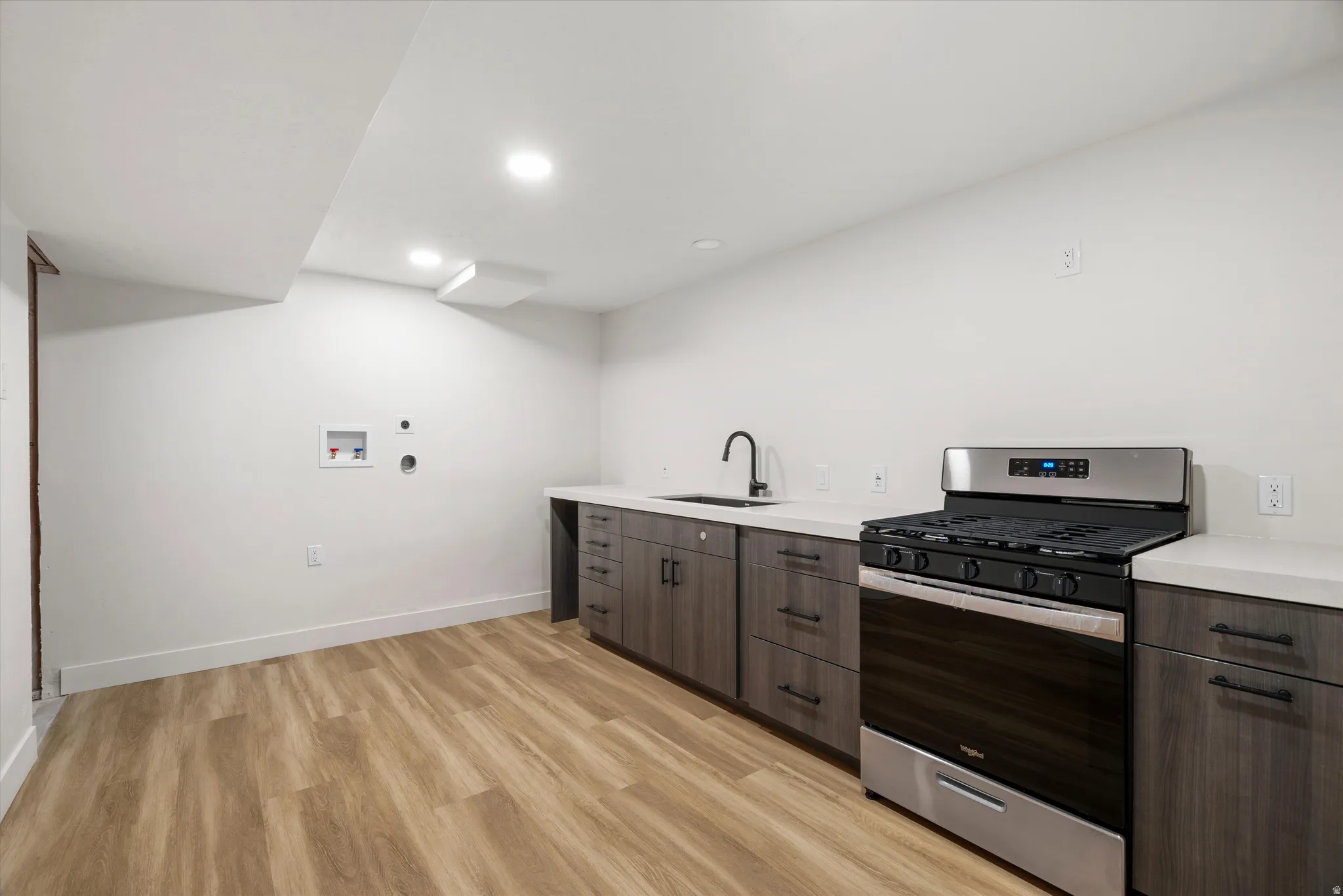 Kitchenette featuring a stainless steel range, wood-finish flooring, recessed lighting, a dark sink with a matte black faucet, and ample cabinetry