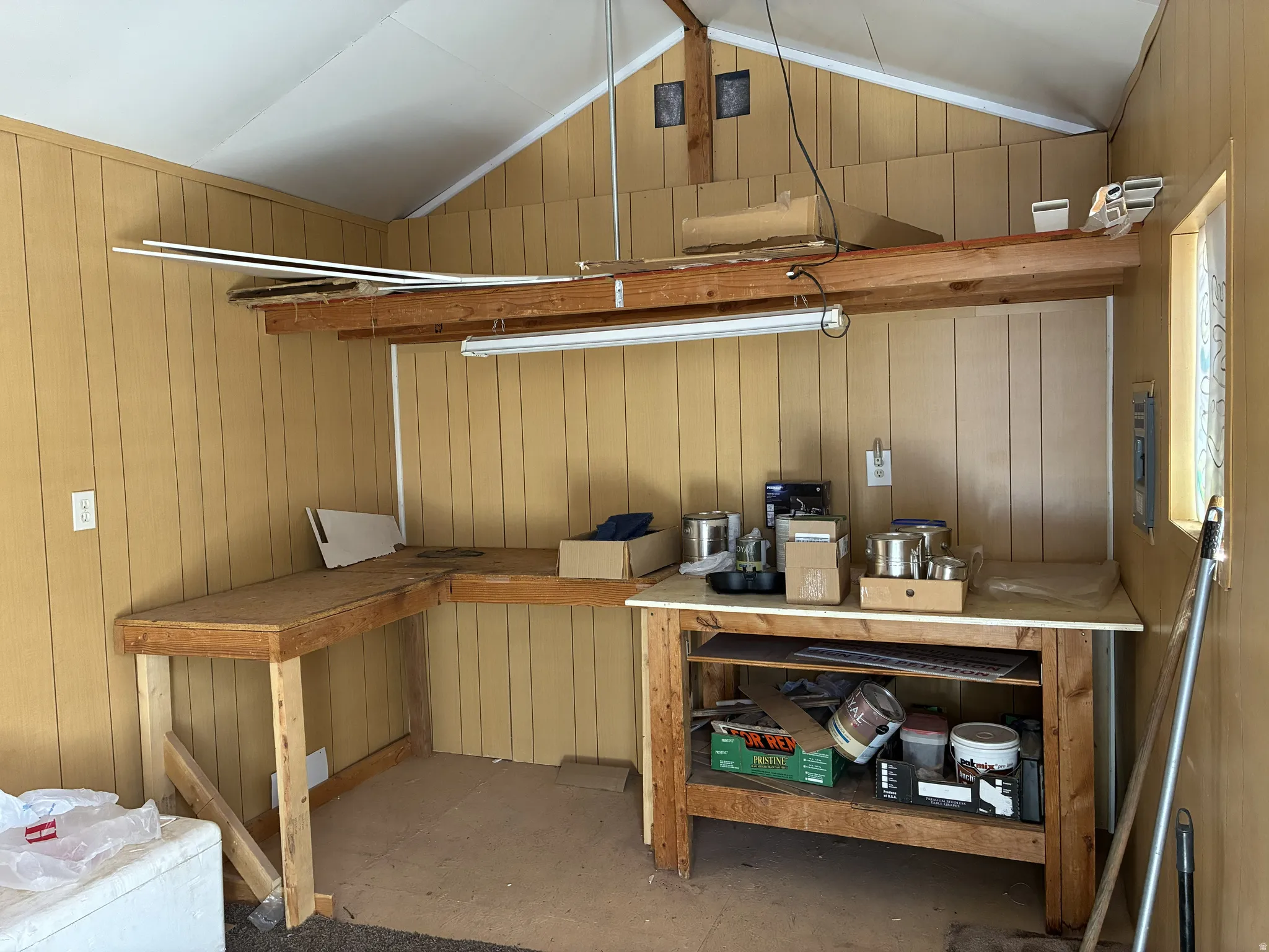 Functional workspace featuring a built-in L-shaped workbench, overhead storage shelf, and vertical wood-paneling walls