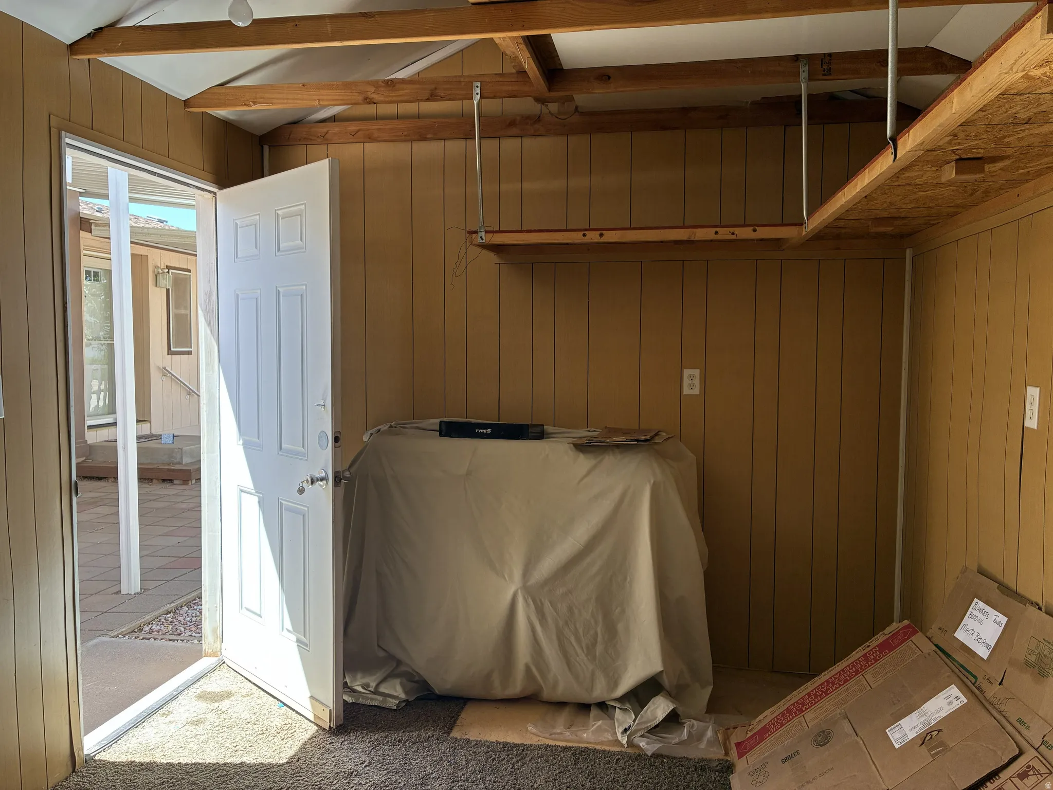 Interior space with wood paneling, open ceiling beams, and overhead shelving