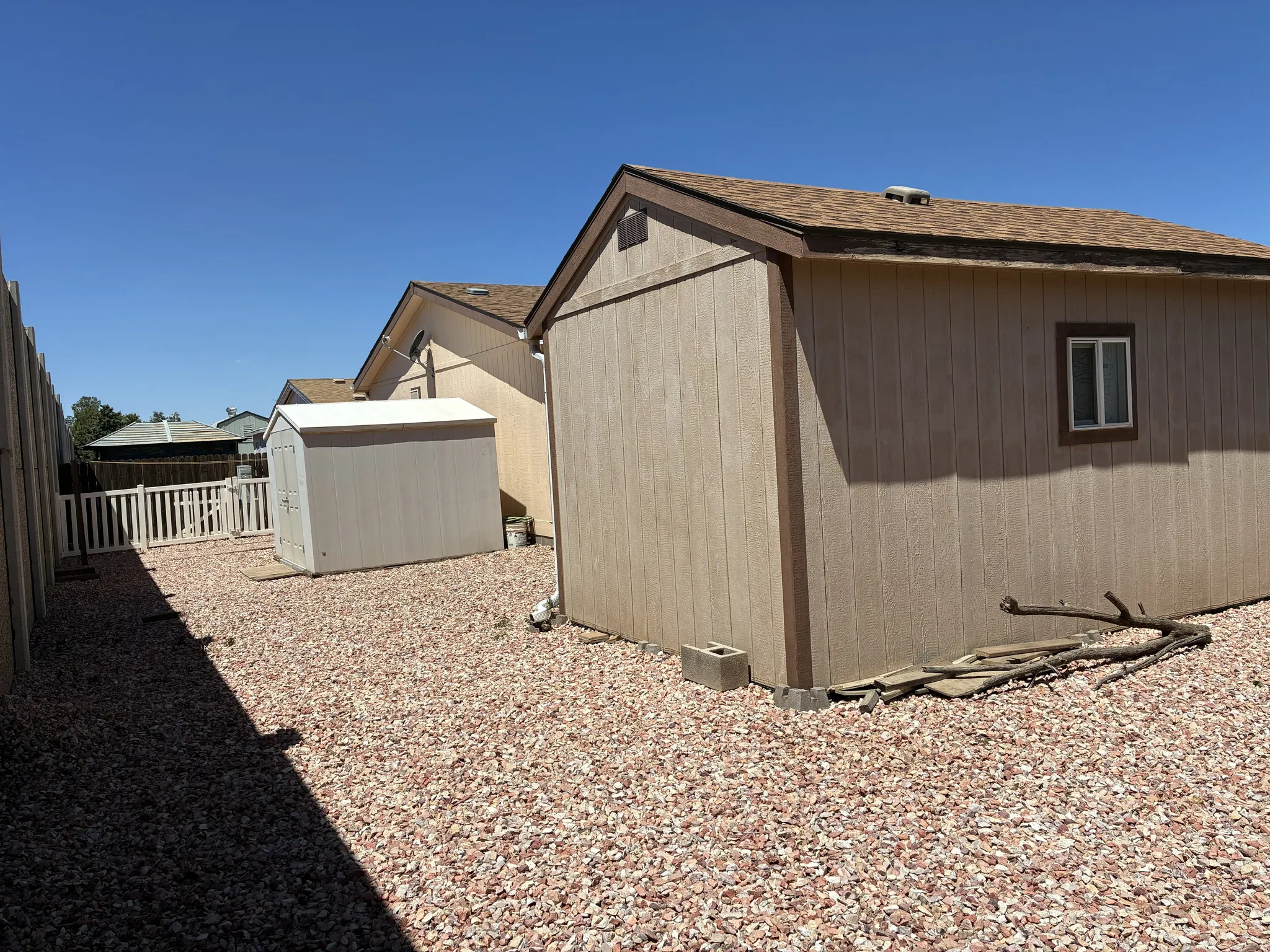Expansive gravel yard featuring a workshop and storage shed, a white picket fence, and a gate