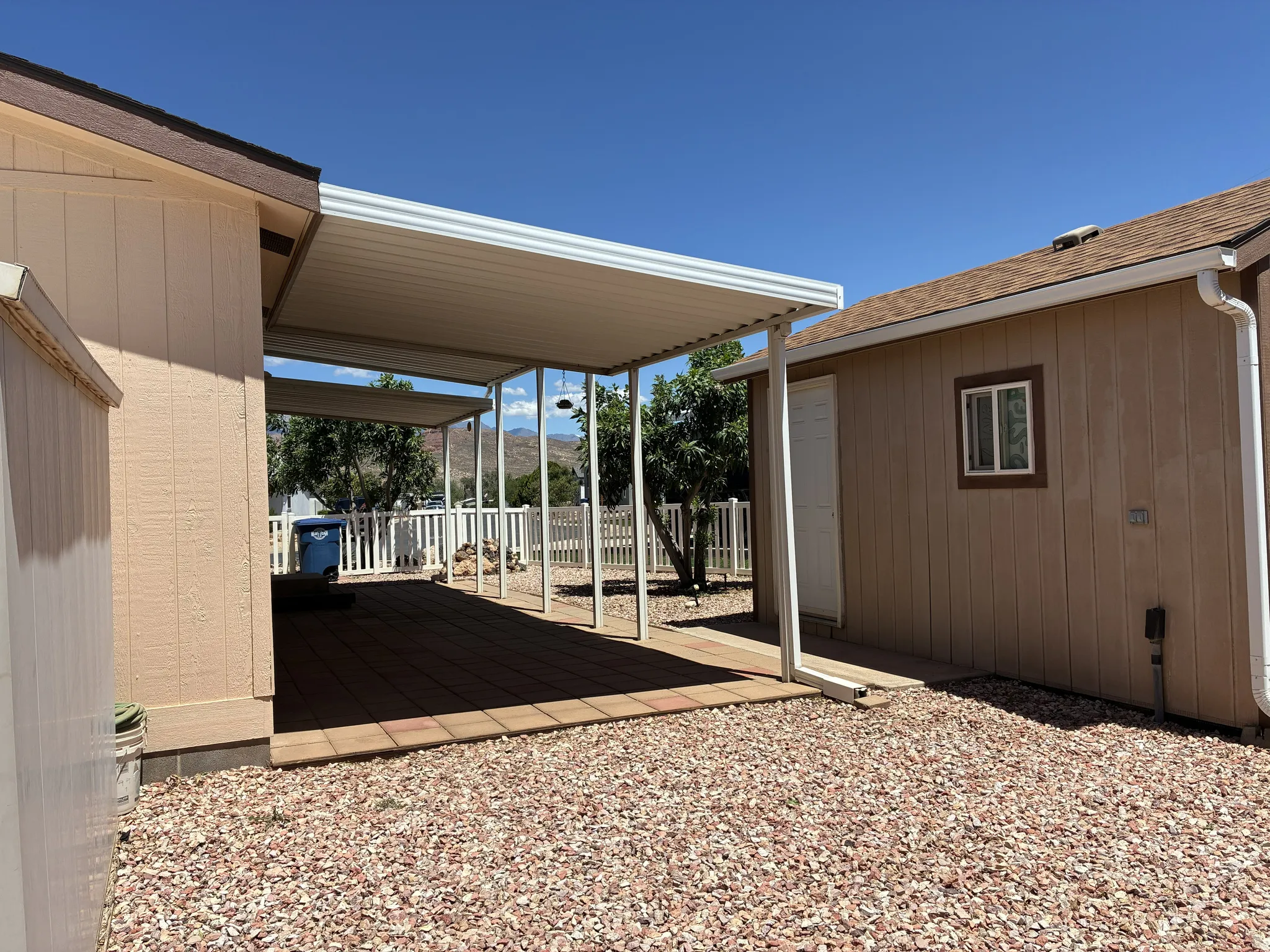 Covered patio area featuring pavers and a white picket fence