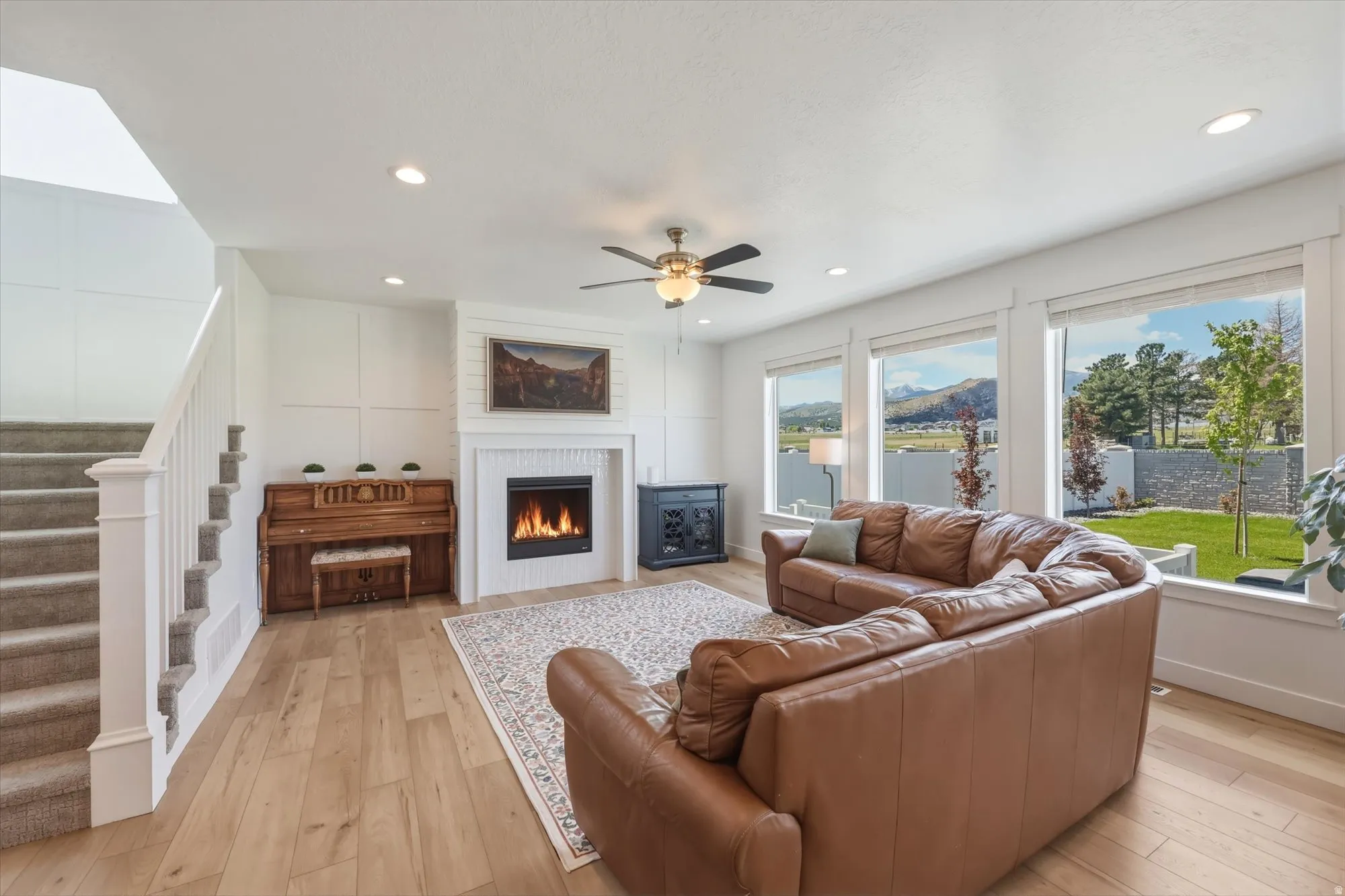 Living space featuring light wood-finish flooring, a contemporary fireplace with white surround, recessed lighting, and a ceiling fan