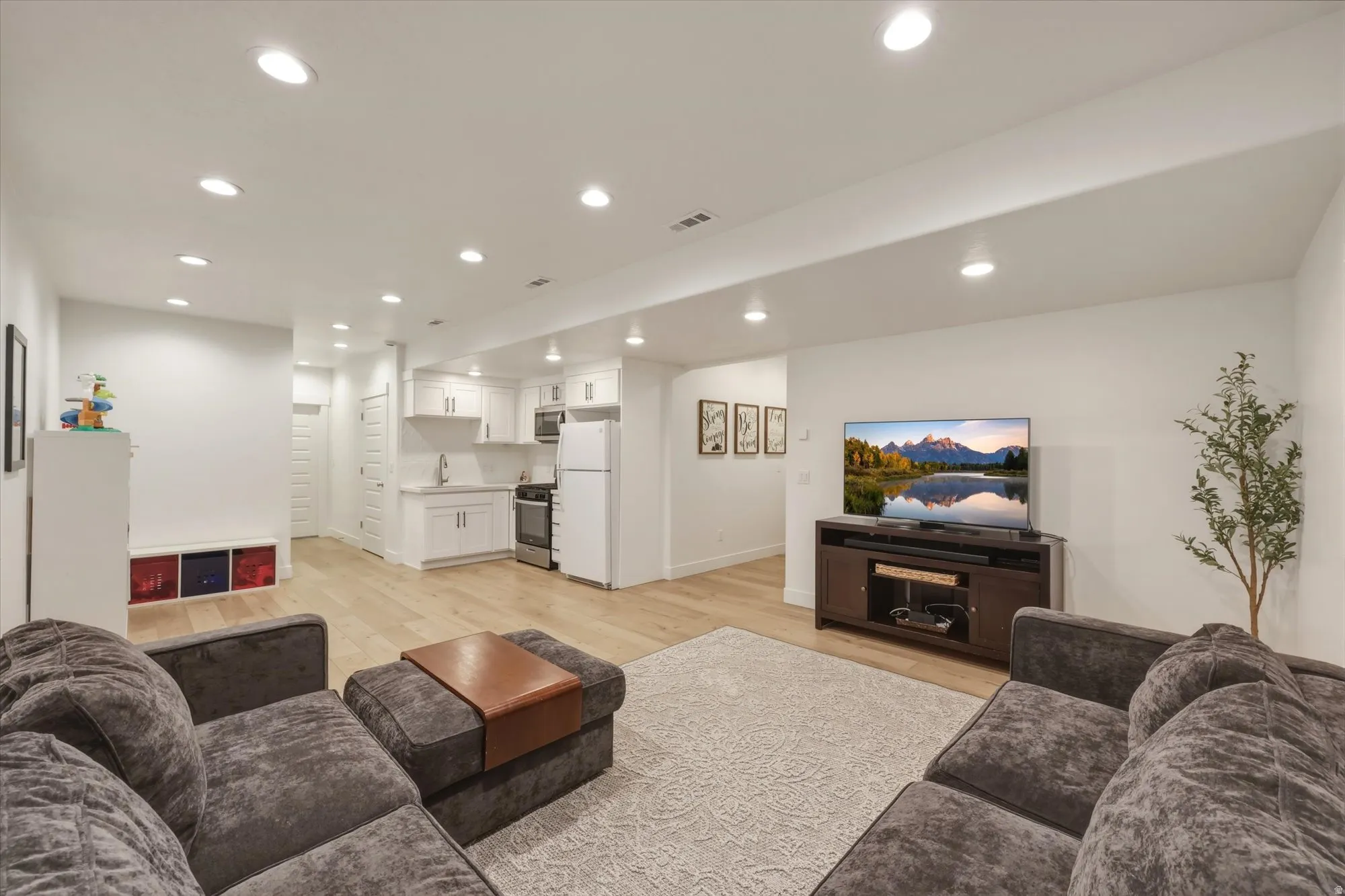 Open-concept living space featuring wood-finish flooring, recessed lighting, and a white kitchen with shaker-style cabinetry, a stainless steel range, and a refrigerator