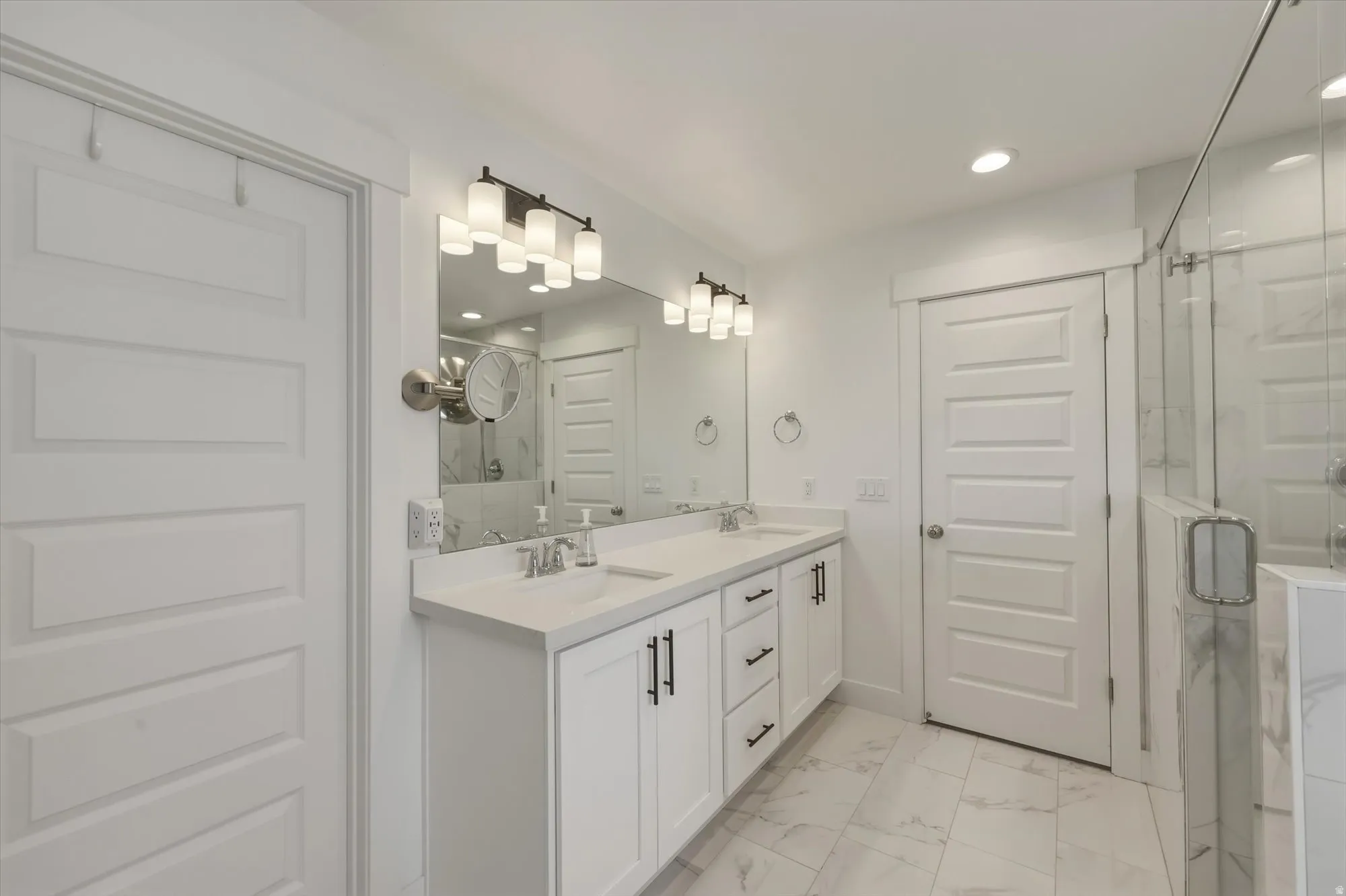 White shaker-style cabinetry with matte black hardware, dual undermount sinks, and a light-toned countertop