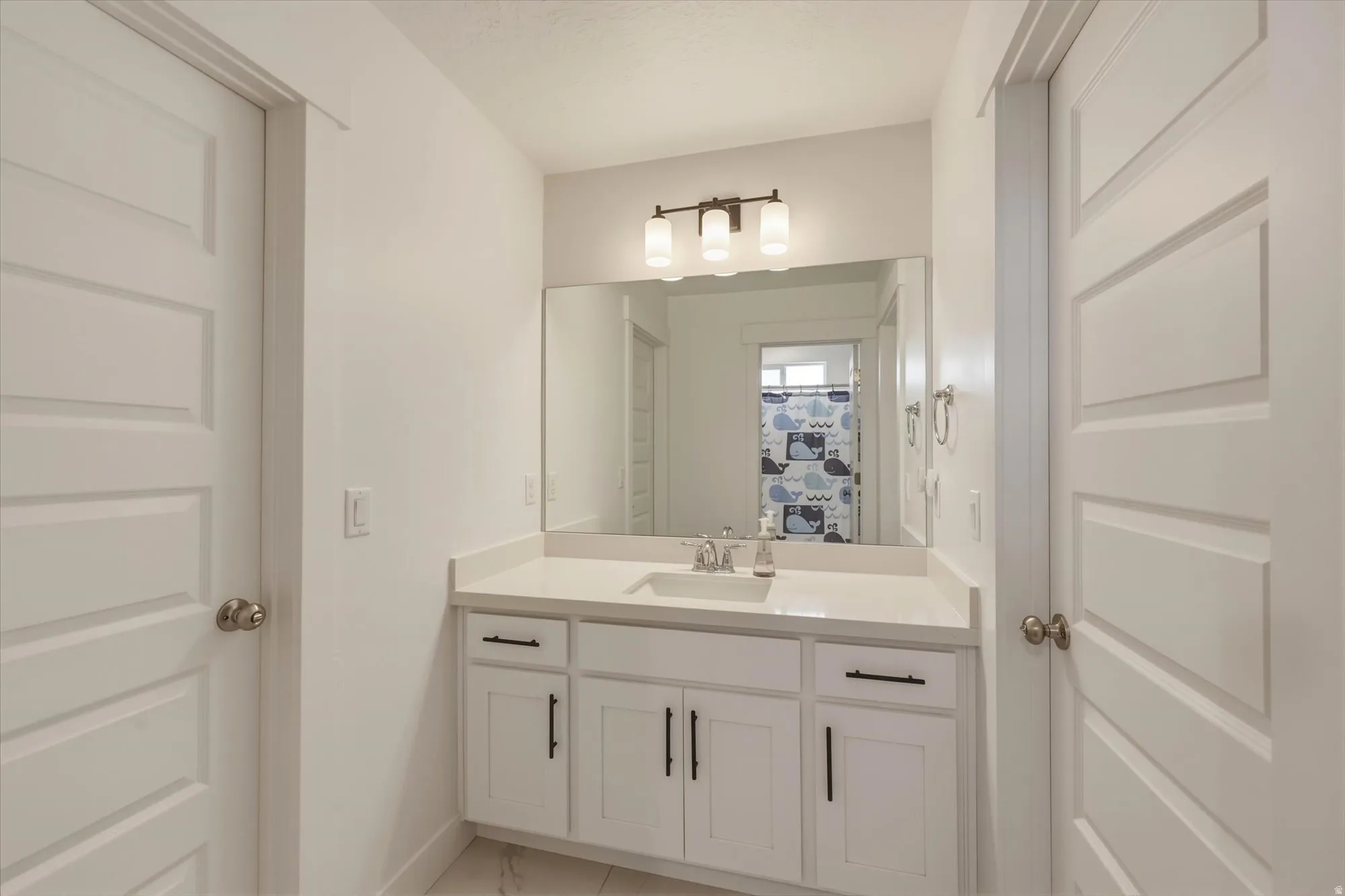 Modern bathroom vanity featuring white cabinetry with black hardware, a light-toned countertop, and an undermount sink with a chrome faucet