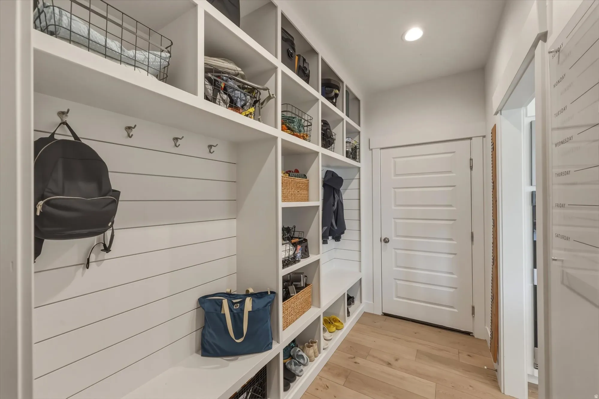 Entryway featuring extensive built-in shelving, integrated coat hooks, shiplap wall accent, a built-in bench, and wood-finish flooring