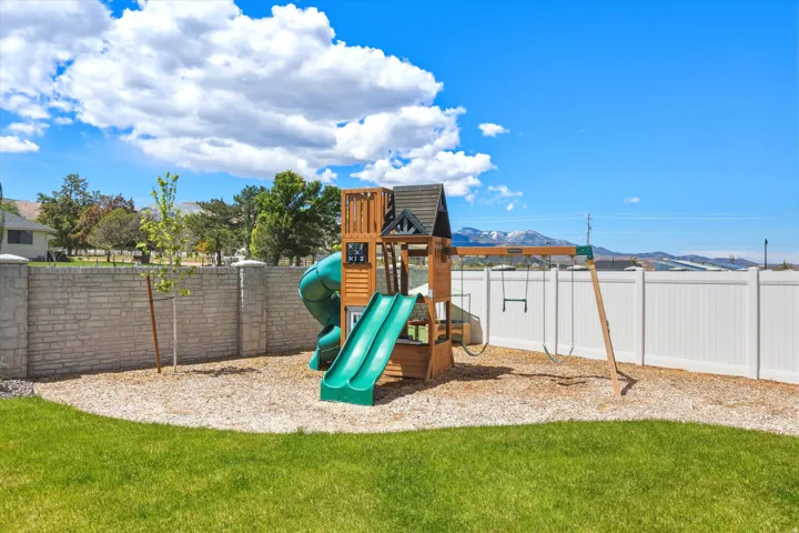 Backyard featuring a wooden play structure with slides and swings, a wood chip base, and a perimeter of green lawn