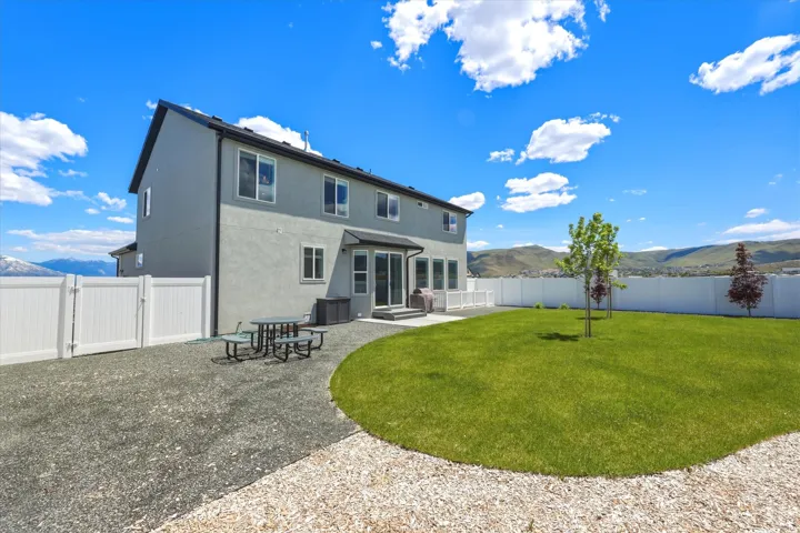 Expansive backyard featuring a manicured lawn, a gravel patio area, a white privacy fence, and a distant mountain backdrop