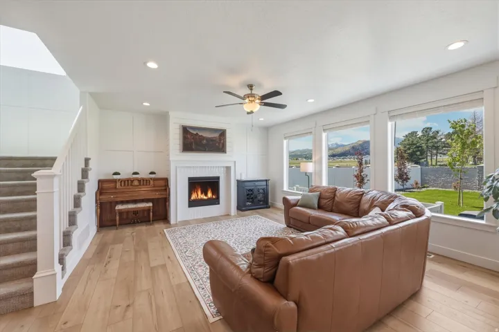 Living space featuring light wood-finish flooring, a contemporary fireplace with white surround, recessed lighting, and a ceiling fan