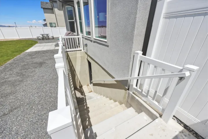 Exterior basement access featuring concrete stairs with a metal handrail, white vinyl railing, and an adjacent white vinyl fence
