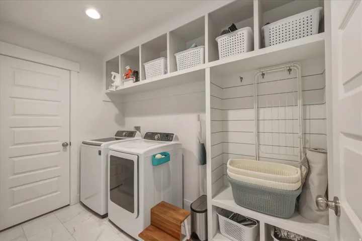 Dedicated laundry area featuring built-in open shelving, white paneled walls, recessed lighting, and large format floor tiles