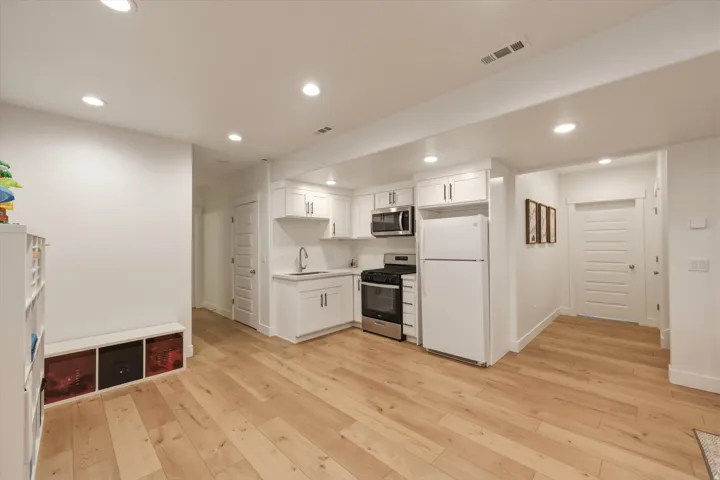 Kitchenette featuring white cabinetry, a stainless steel range, a white refrigerator, and wood-finish flooring