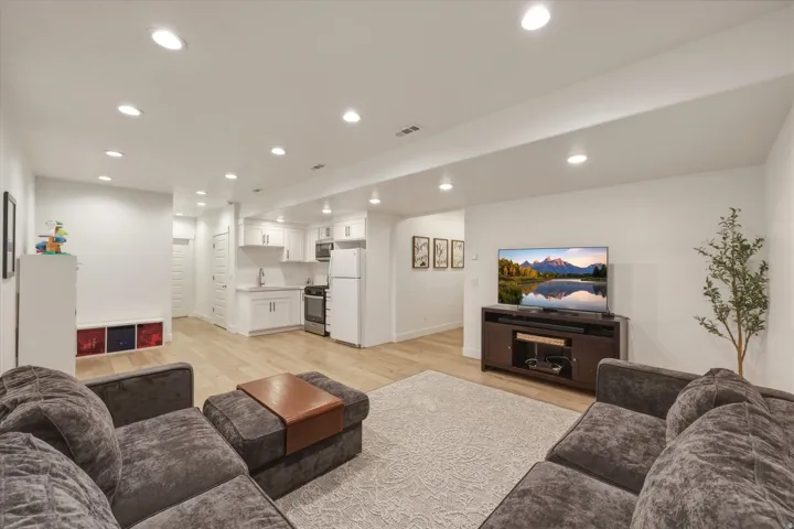 Open-concept living space featuring wood-finish flooring, recessed lighting, and a white kitchen with shaker-style cabinetry, a stainless steel range, and a refrigerator