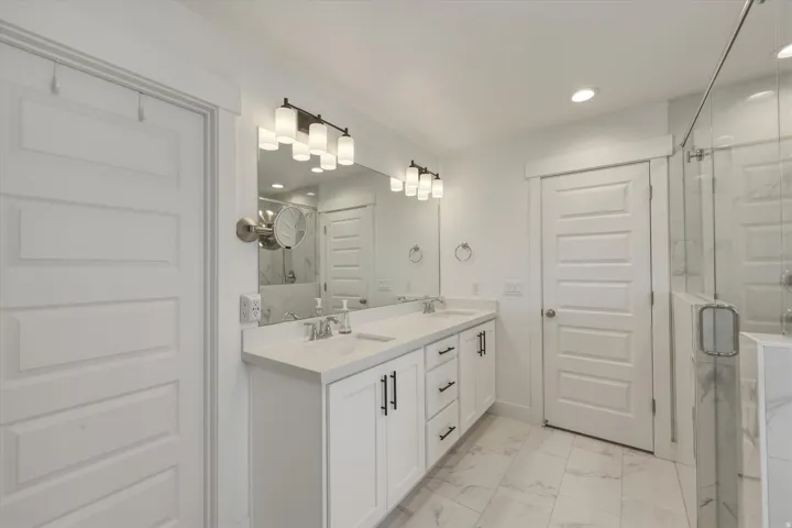 White shaker-style cabinetry with matte black hardware, dual undermount sinks, and a light-toned countertop