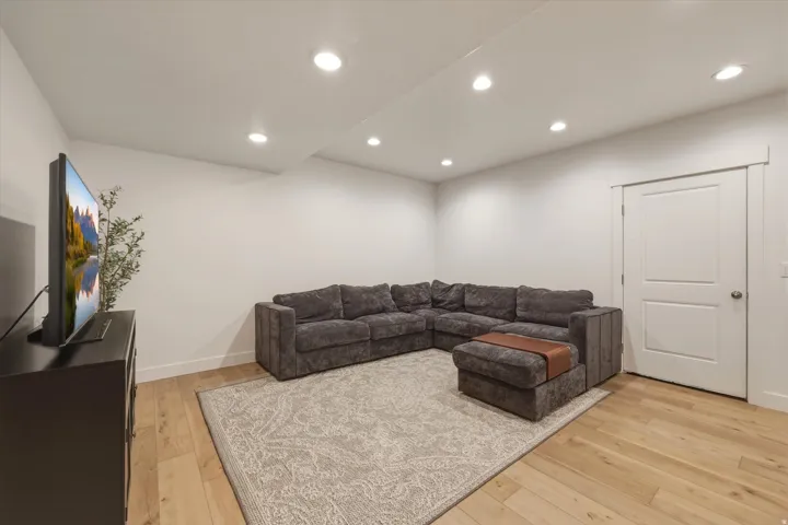 Recessed lighting illuminates this room featuring wood-finish flooring, white walls, and a two-panel interior door with brushed nickel hardware