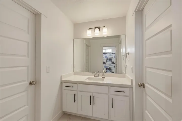 Modern bathroom vanity featuring white cabinetry with black hardware, a light-toned countertop, and an undermount sink with a chrome faucet