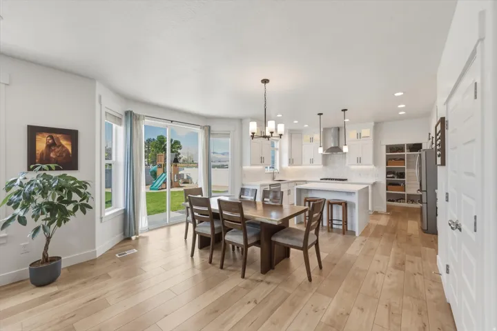 Open-concept living area featuring light wood-finish flooring, a contemporary kitchen with white cabinetry, a kitchen island with seating, pendant lighting, and a dining area with a modern chandelier