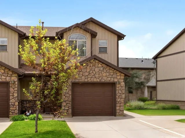 Stone-accented townhome with an integrated garage, arched window, and a neatly maintained lawn