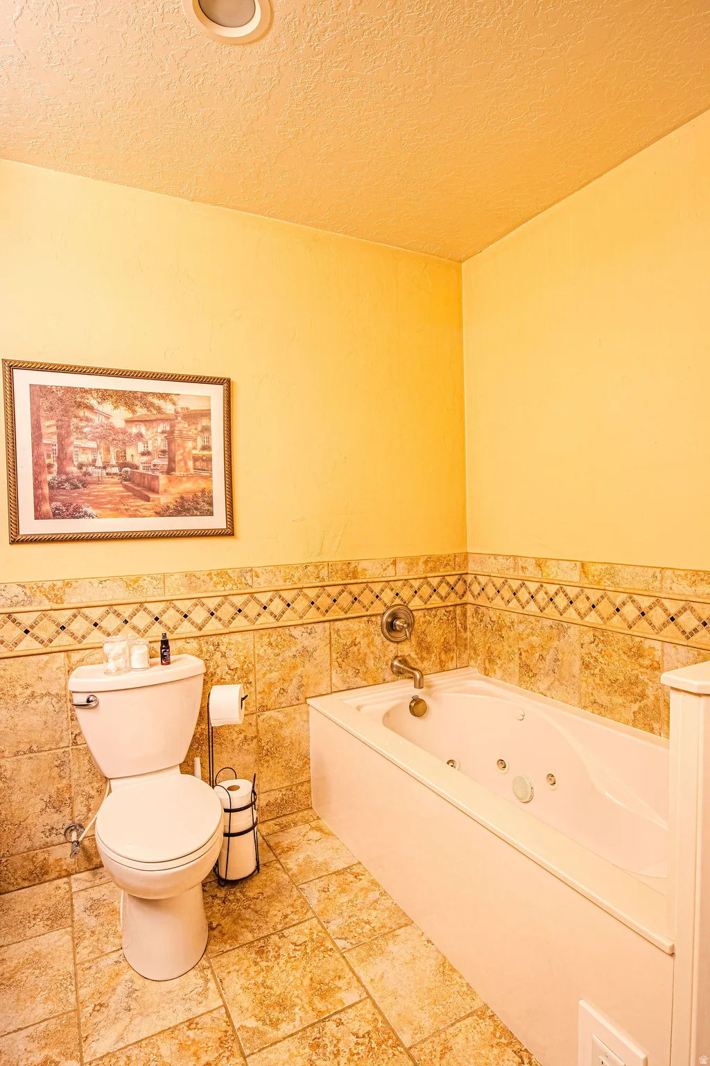 Master bathroom featuring a jetted tub, ceramic tile flooring, and coordinating tiled wainscoting with a decorative border