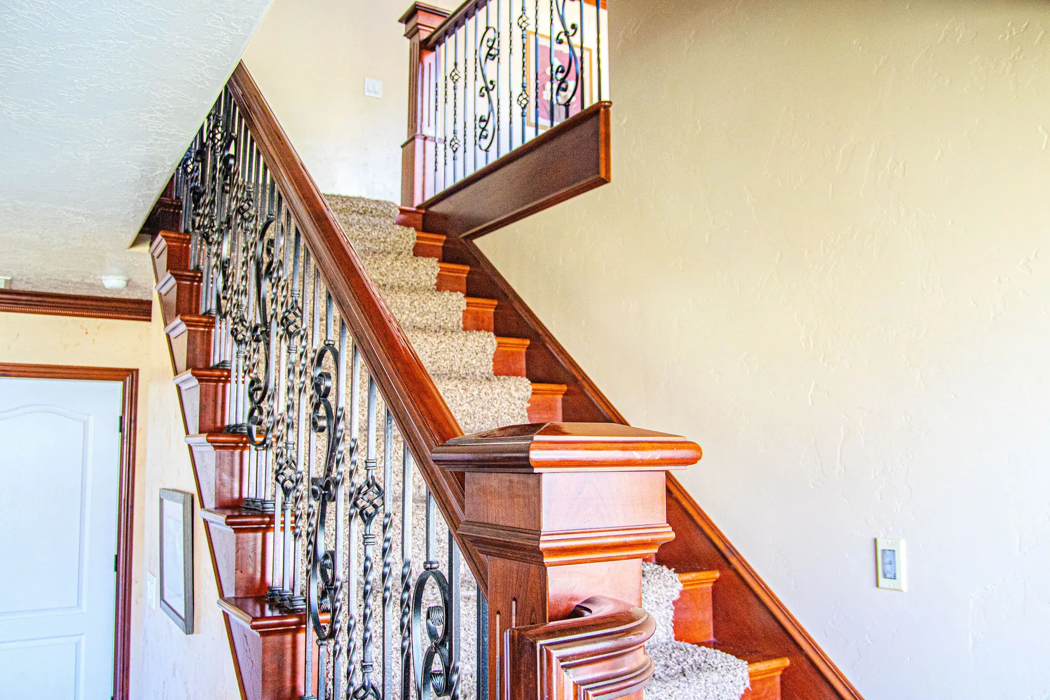 Ornate staircase featuring decorative wrought iron balusters, dark wood newel posts, and carpeted treads