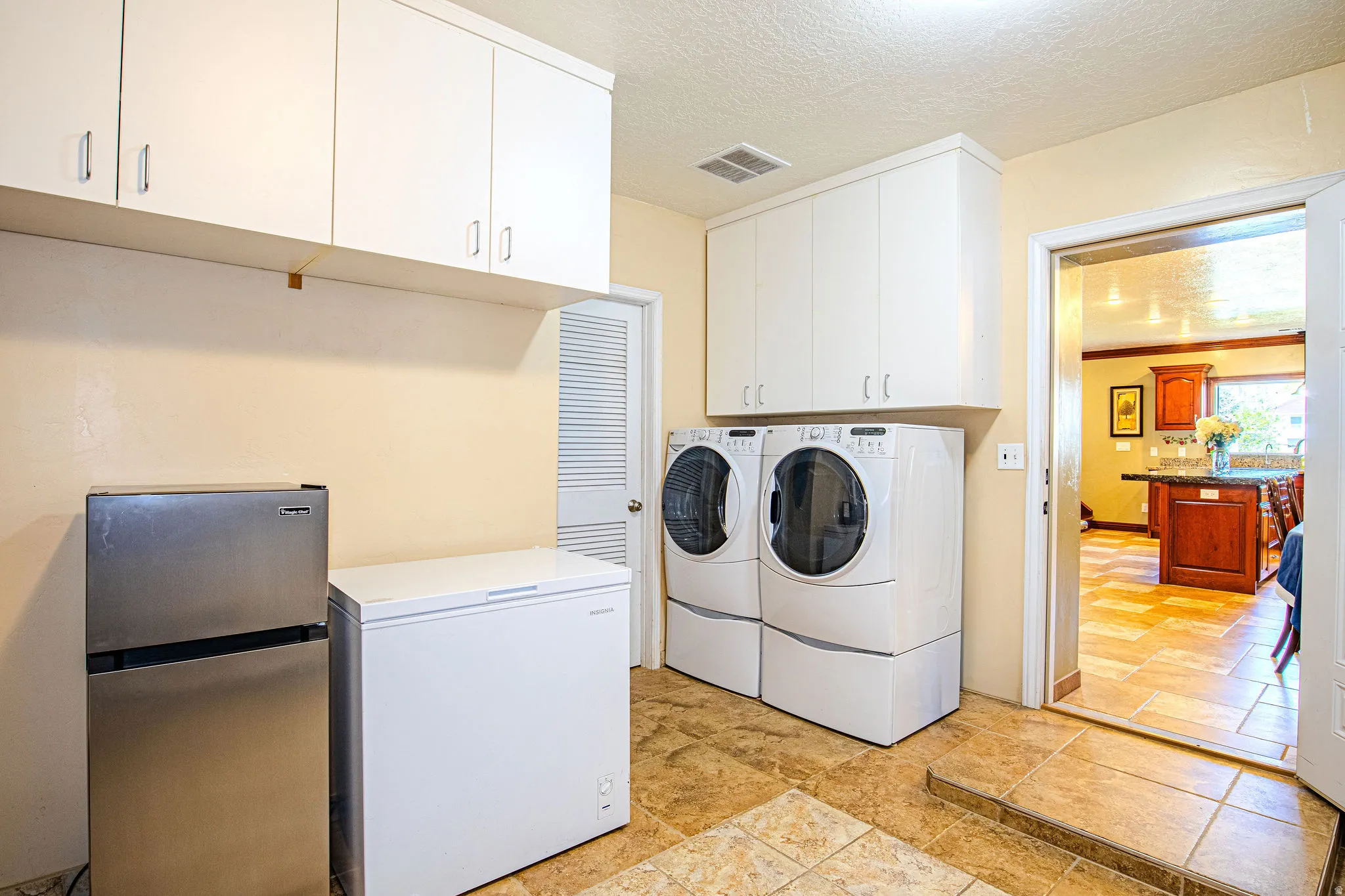 Utility room featuring ample white cabinetry, tile flooring, and a louvered door. Pantry