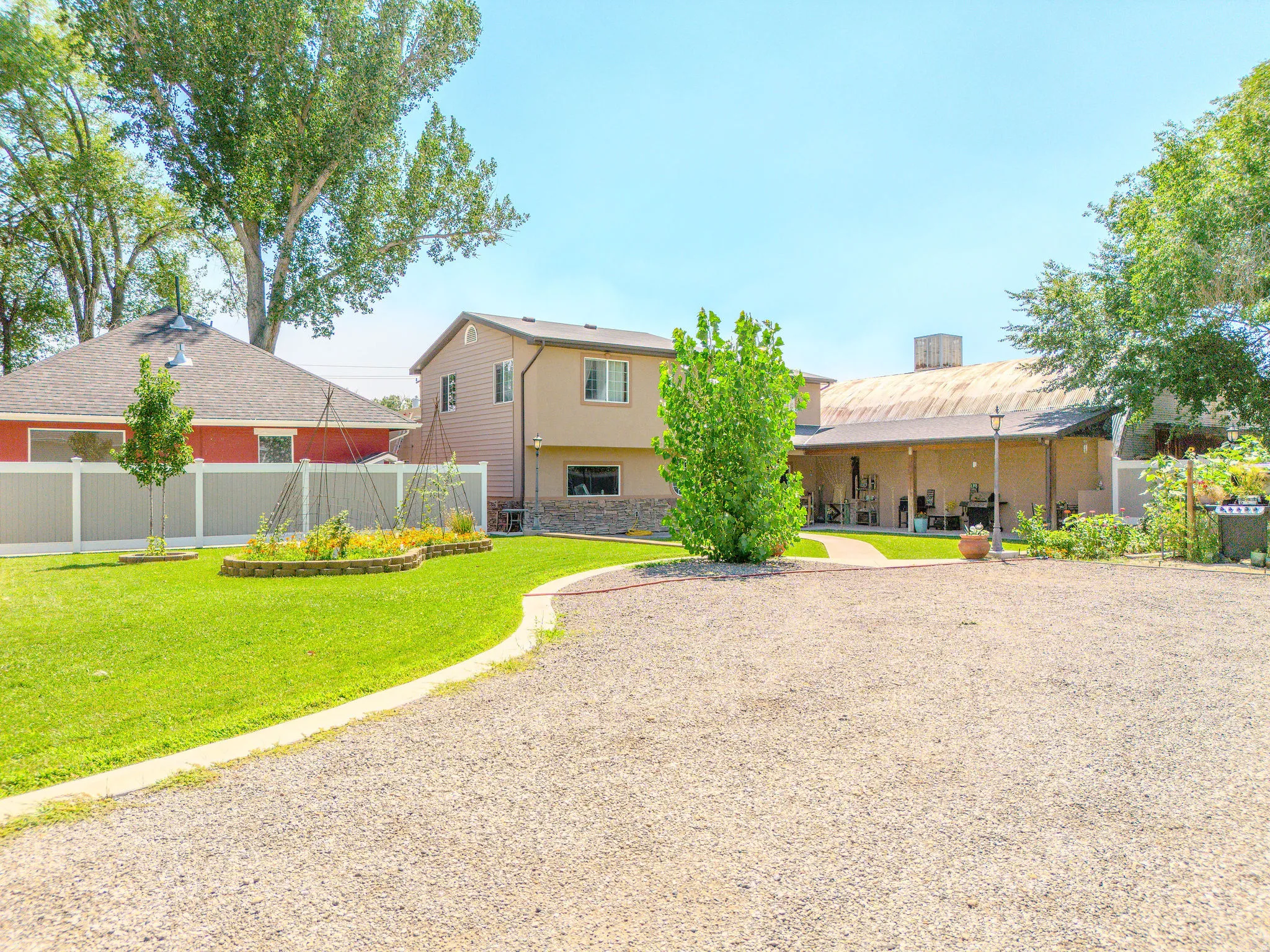 Gravel driveway leading to a manicured lawn, established garden beds, and two-story exterior with stone accents
