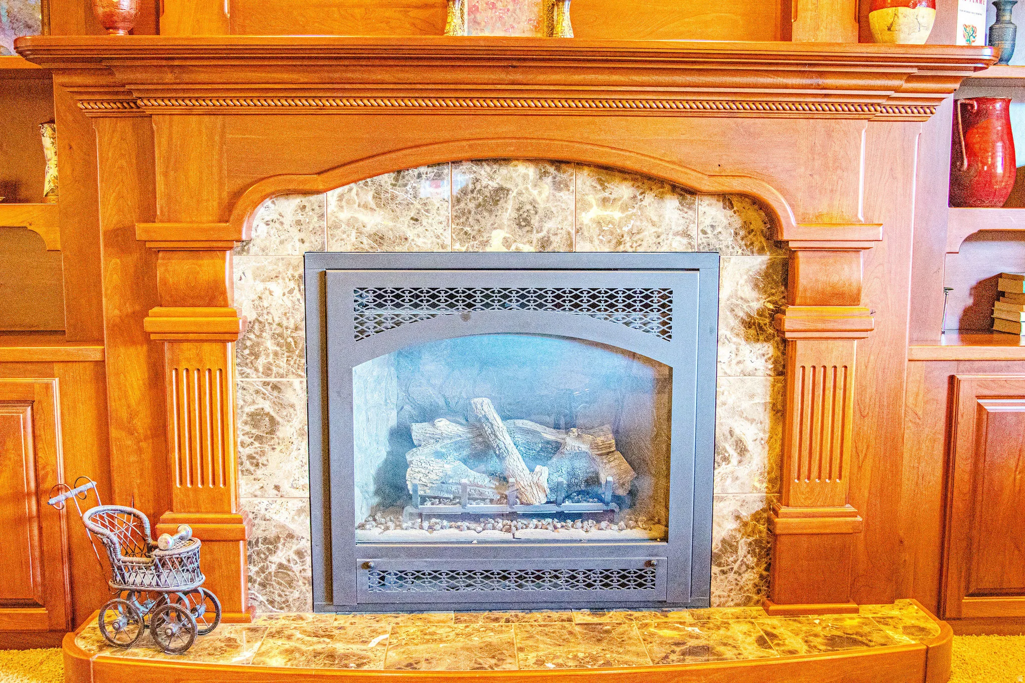 Built-in fireplace featuring a stone surround, decorative metal screen, and a wood mantel with fluted columns and carved detailing