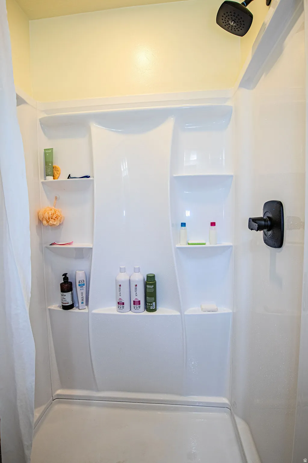 White shower enclosure featuring built-in shelving, matte black fixtures, and a shower curtain rod
