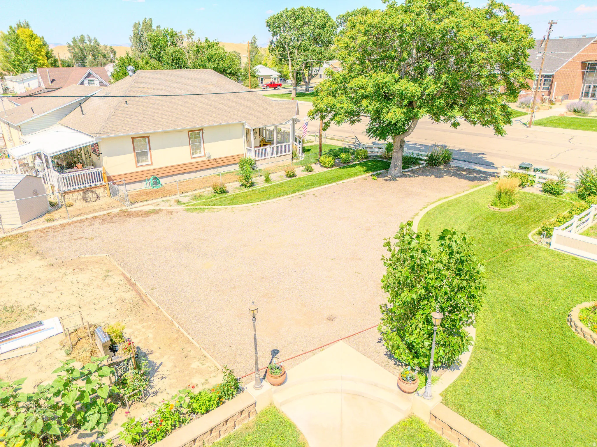 Spacious gravel lot, expansive green lawn, mature trees, white picket fencing, and a covered porch