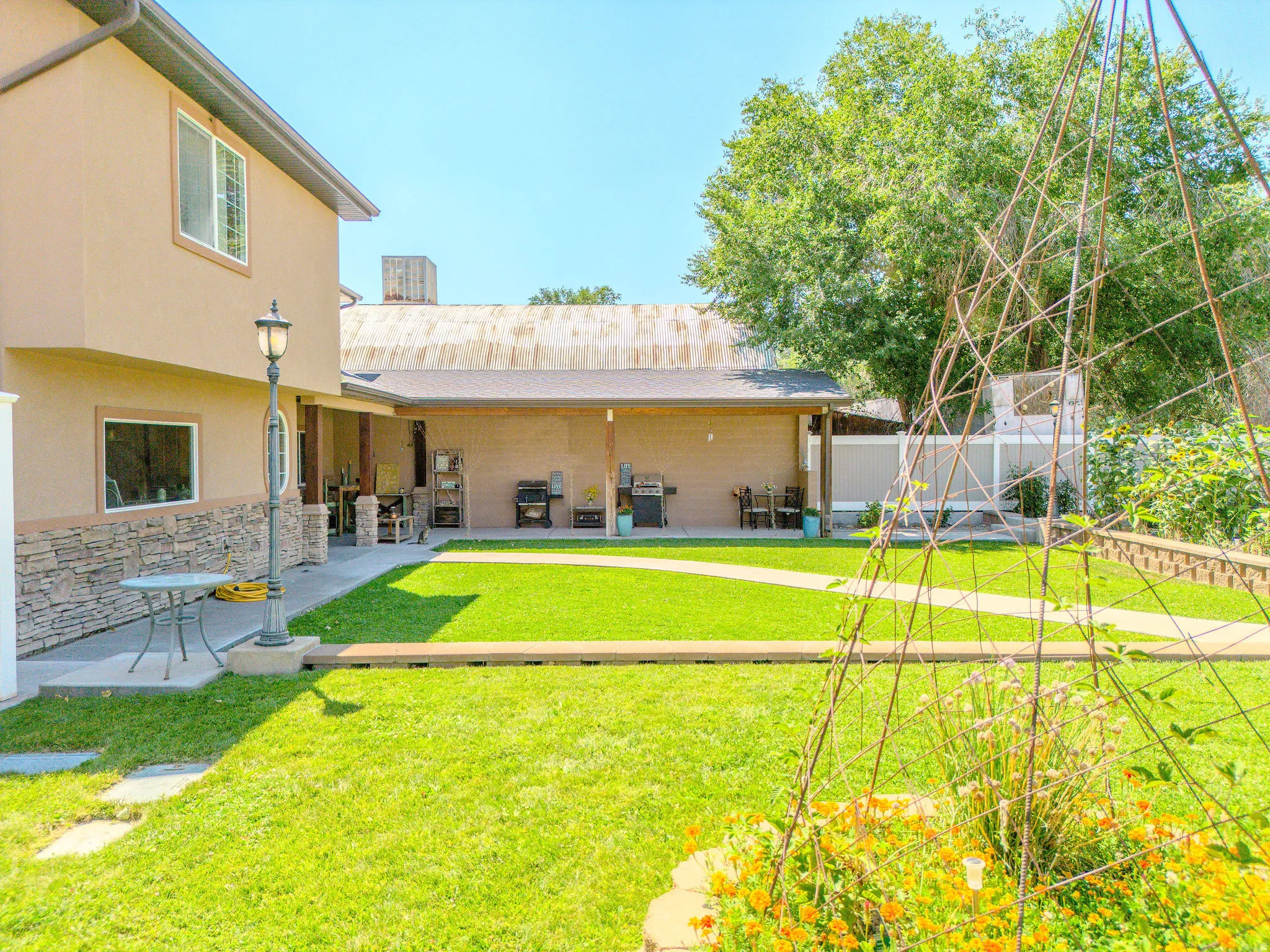 Expansive green lawn with a defined pathway, stone-clad exterior accents, covered patio, and garden features