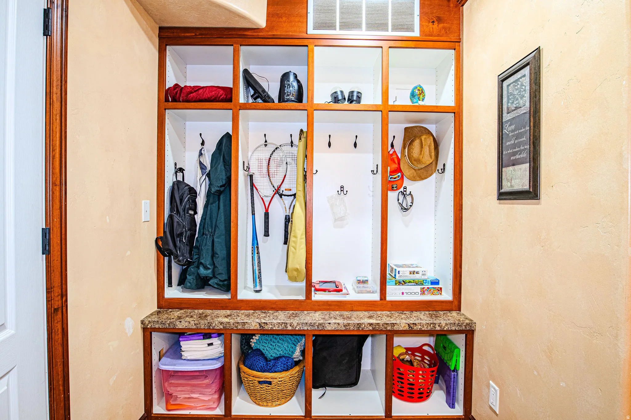 Built-i  organization system featuring wood-finish framing, integrated seating with a stone-finish countertop, upper and lower storage cubbies, and multiple coat hooks