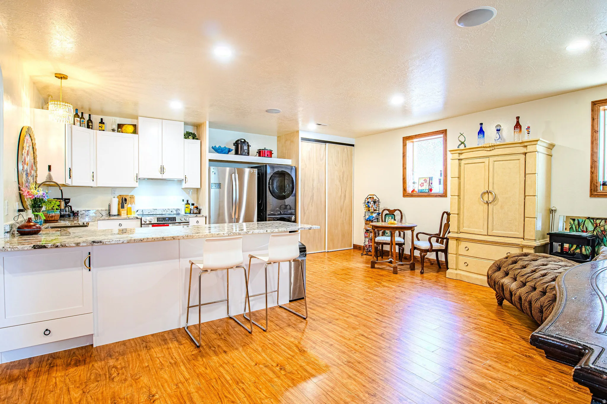 Bright open-concept kitchen featuring white cabinetry, granite-style countertops, stainless steel appliances, and a breakfast bar