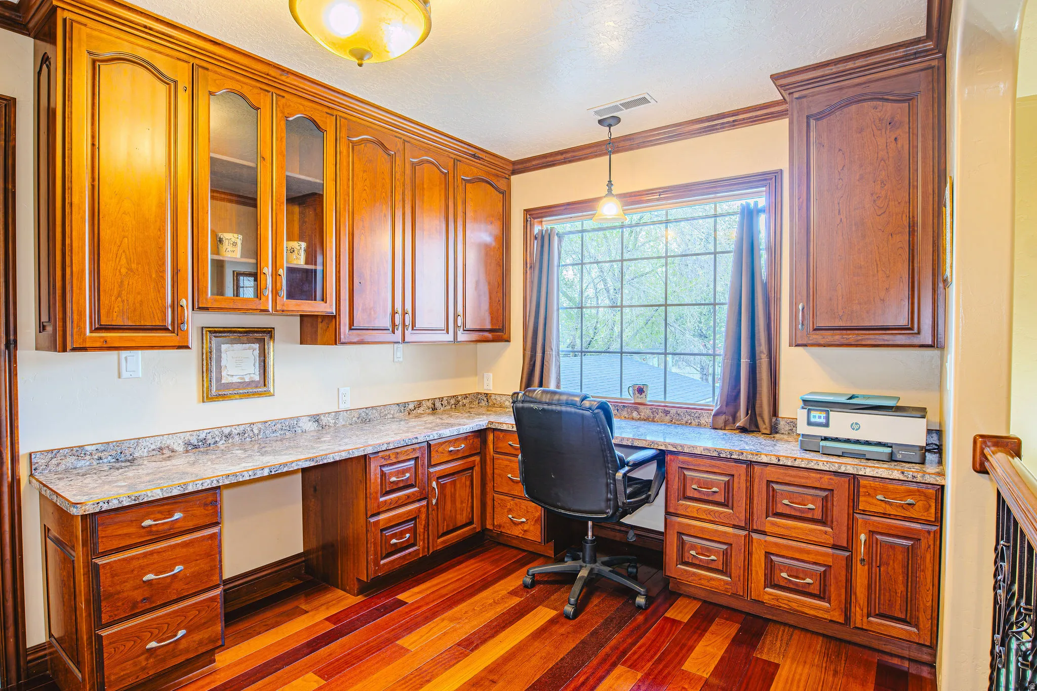 Built-in desk area featuring wood cabinetry, stone countertops, wood-finish flooring, a pendant light fixture, and a window