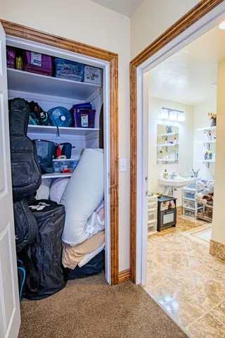 Functional hallway featuring a built-in closet with shelving and warm wood-finish trim, with a bathroom entry showcasing tile flooring. This is in the entry/hallway to second living space.