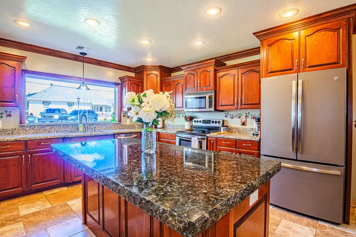 Kitchen featuring a large island with a speckled countertop, extensive wood cabinetry, stainless steel appliances, recessed lighting, and tile flooring