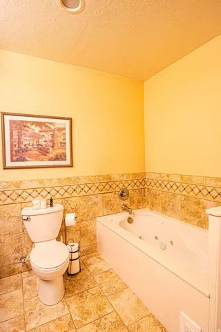 Master bathroom featuring a jetted tub, ceramic tile flooring, and coordinating tiled wainscoting with a decorative border