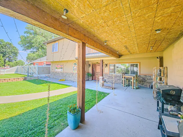 Covered patio with an exposed wood ceiling and recessed lighting, featuring a concrete floor and stone accent wall