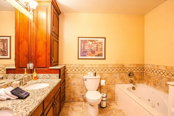 Master bathroom featuring a jetted tub, a vanity with a granite countertop, a built-in wood-finish cabinet, and a tiled shower surround