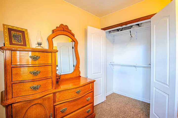 Carpeted closet with double white bi-fold doors, white shelving, and a hanging rod. Beautiful antique wood dresser
