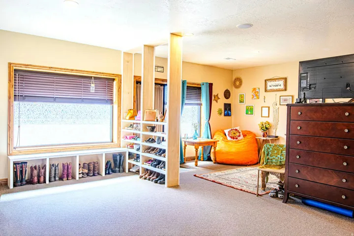 Carpeted room featuring a built-in window bench with storage, a large window with blinds, and a partial room divider with shelving