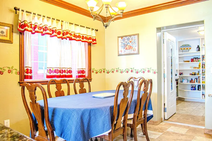 Dining area featuring a decorative chandelier, crown molding, and a window with wood trim. Entrance to pantry and laundry room in background