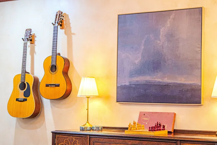 Warm-toned wall featuring a large abstract art piece, two wall-mounted guitars, and a decorative table lamp